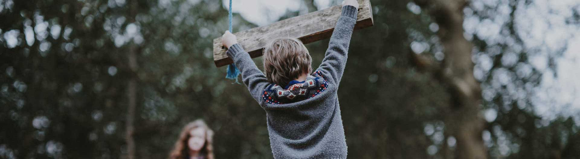 boy in sweater hanging from wooden swing