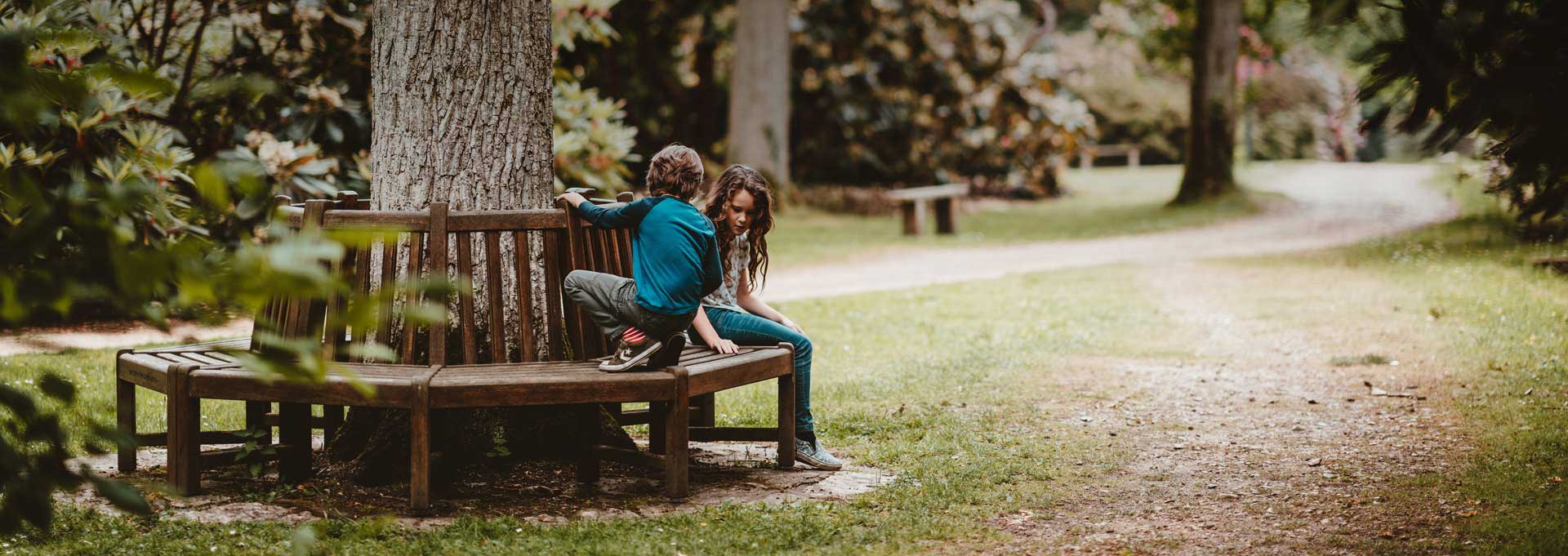 boy and girl sitting on bench surrounding tree in park